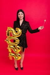 A young woman in a shiny dress and high-heeled shoes holds the numbers 2022 and a sparkler