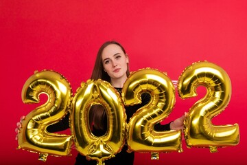 A happy brunette in a black dress holds the numbers 2022 on a red background