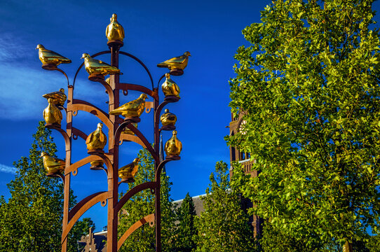 Weesp, northern Netherlands - June 23, 2017. Golden metal birds monument with leafy tree in sunny day at Weesp. Quiet and pleasant village full of canals and green near Amsterdam