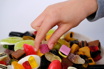 close-up of child's hand taking one gelatin candy, gummy bear, colored gelatinous sweets, black...