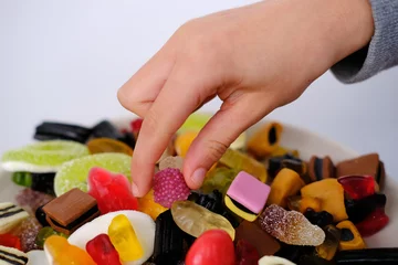 Abwaschbare Fototapete close-up of child's hand taking one gelatin candy, gummy bear, colored gelatinous sweets, black licorice candies, unhealthy food concept, halal gelatin, selective focus at shallow depth of field © kittyfly