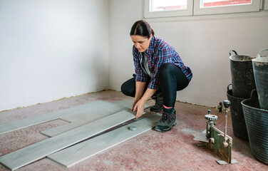 Crouched female bricklayer placing tiles to install a floor