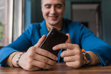 Close-up, businessman guy holds a black smartphone or mobile phone in his hand and takes a selfie or talks on a video link in a cafe