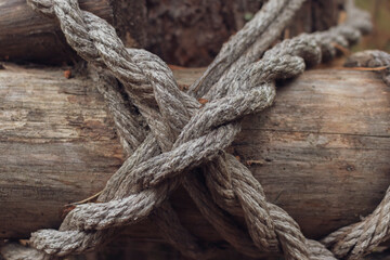 Fototapeta na wymiar Wooden logs are fastened with a twisted rope criss cross, close-up. This shot symbolizes strength, reliability and confidence.