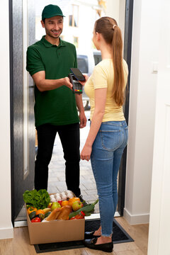 Smiling deliveryman with credit card reader  receiving payment from customer at doorway