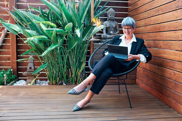 Mature businesswoman using digital tablet while sitting on chair in backyard