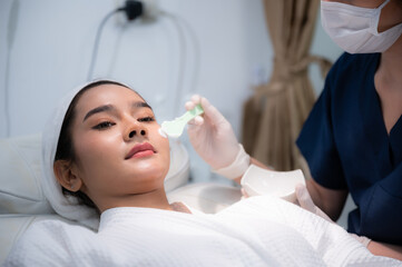 Naklejka premium young Asian woman making treatment cosmetic beauty therapy on a face at cosmetological clinic