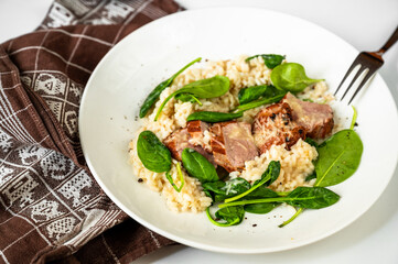 Pork tenderloin medallions on risotto with parmesan and spinach leaf on white plate and towel.