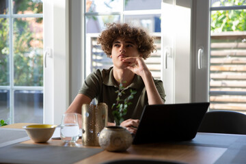 Teenage boy contemplating while sitting with laptop at home