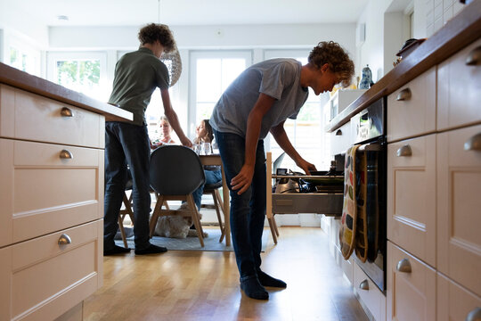 Boy searching in drawer while family at dining table - Powered by Adobe