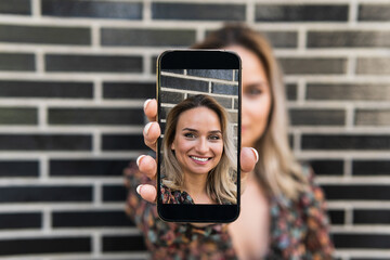 Young woman showing photograph on smart phone while standing in front of wall