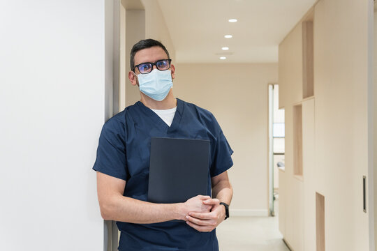Male dentist wearing protective face mask standing with file at clinic