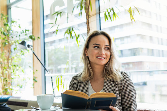 Smiling businesswoman with book looking away while sitting at cafe