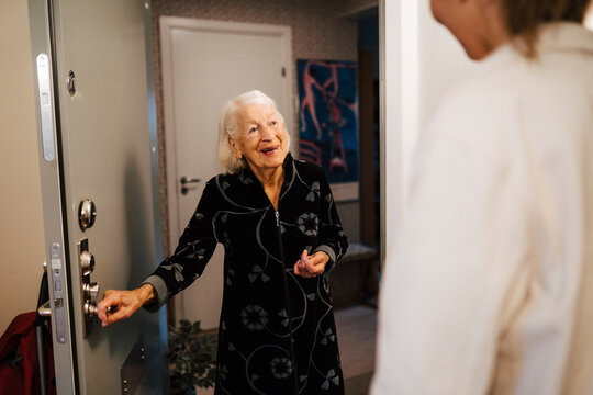 Smiling senior woman opening door while female nurse arriving at home