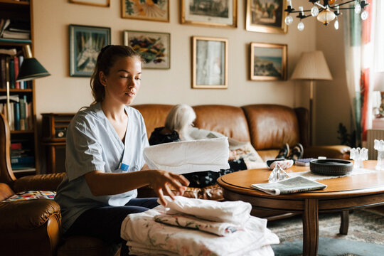 Female caregiver arranging blankets while senior woman sitting in background at home