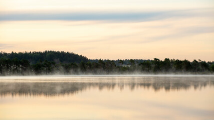 Fog rising slowly on the lake during early morning sunrise at Kakerdaja bog in Estonia, Northern Europe