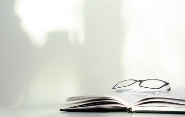 The open diary lies on a white background, which is illuminated by the sun. On the pages lie white rimmed glasses