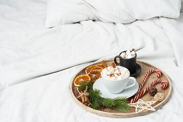 Winter holiday mood. Two coffee cup with marshmallow, candy cane, Christmas decorations on the bed. Christmas morning, coffee time.