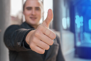 A young man shows a close-up of a thumbs up class against a street outdoor background