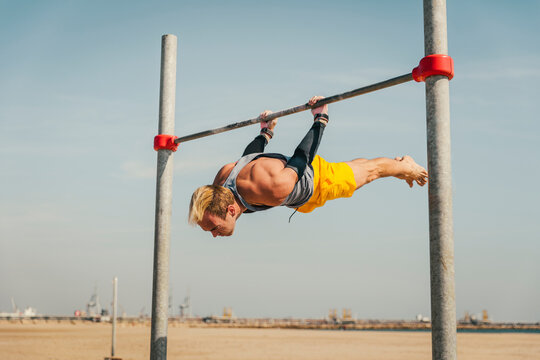 Male athlete exercising on high bar during sunny day