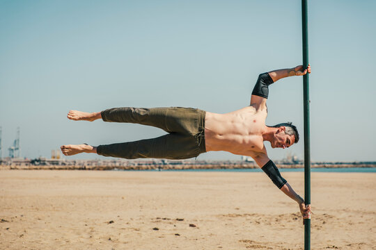 Male sportsperson doing exercise while balancing on bar at beach