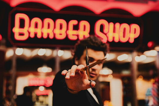 Young male hairdresser showing scissor outside barber shop
