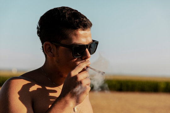 Young man with eyeglasses smoking marijuana joint