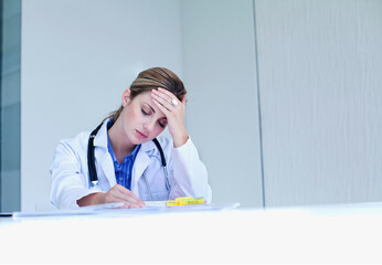 Stressed female doctor with head in hand sitting at desk in hospital