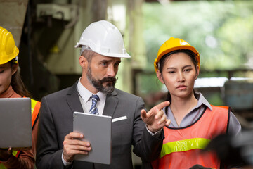 Male engineer and Industrial workers in Hard Hats Discuss New Project while Using Laptop. They Make Showing Gestures.They Work in a Heavy Industry Manufacturing Factory.