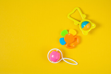 Top view a colorful baby rattle on yellow background with copy space. Flat lay newborn rattle toy on colored background. Baby toys concept