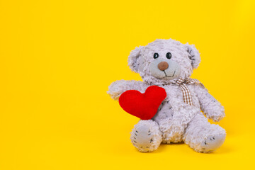baby bear toy on a yellow background with copy space. gray bear toy with heart on a colored background. Stuffed animal. Baby toys concept