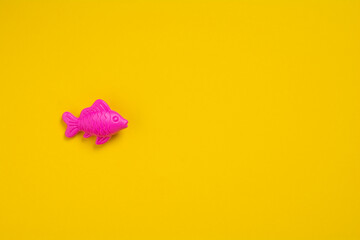 Figure of plastic fish on a yellow background with copy space. Flat lay pink fish on a colored background. Healthy eating concept. Baby toys concept.