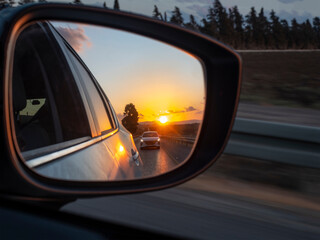 The sunset is reflected in the mirror of a car racing down the highway