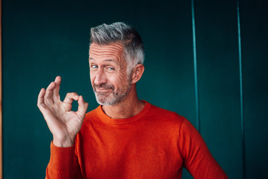Mature man gesturing OK sign in front of wall