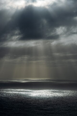 Naklejka na ściany i meble Sunlight through dark rainy clouds at ocean.