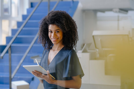 Smiling Afro female professional with digital tablet standing by steps in industry