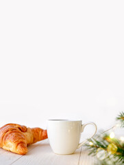 Cup of coffee or tea with croissant and christmas decor on white background, vertical photo with copy space