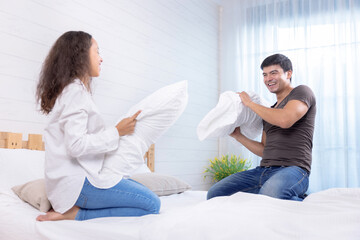 Happy family, Happy young couple playing pillow fight on the bed on weekend morning, Spending time together in family.