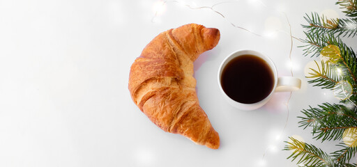 Cup of coffee with croissant and branches of christmas tree on white wooden background