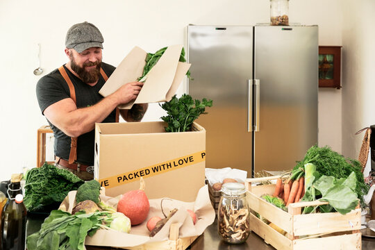 Mature man with delivery service packing organic vegetables in cardboard