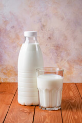 Bottle and glass of milk on a brown wooden table. Food background, cooking ingredient, drink. Healthy food, a source of calcium.