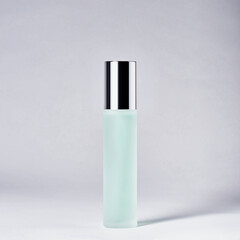 Colored cosmetic in glass bottle with chrome cap on gray background