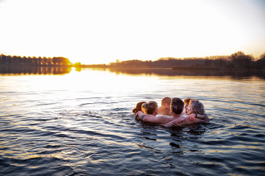 Male and female friends with arms around talking in water