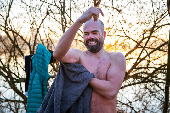 Bearded man cleaning body with towel in front of bare tree