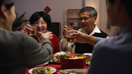 over shoulder shot with selective focus senior couple grandfather and grandmother making toast to family members, celebrating spring festival while having big meal on new year's eve