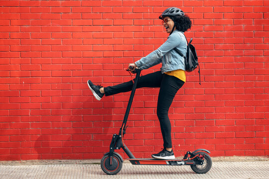 Carefree woman riding electric push scooter by red brick wall