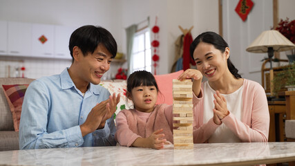 happy asian parents clapping hands and praising their daughter who did good job in playing toy wood blocks while they spending time together on chinese new year at home