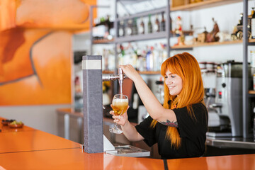 Smiling redhead waitress filling beer glass from tap at bar