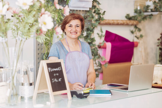 Smiling mature female florist standing at checkout in flower shop