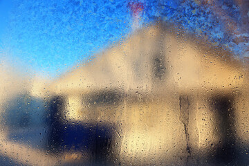 View of house on street from inside through misted glass of window with drops of water. Abstract background. Blurry image. Effect of defocus.